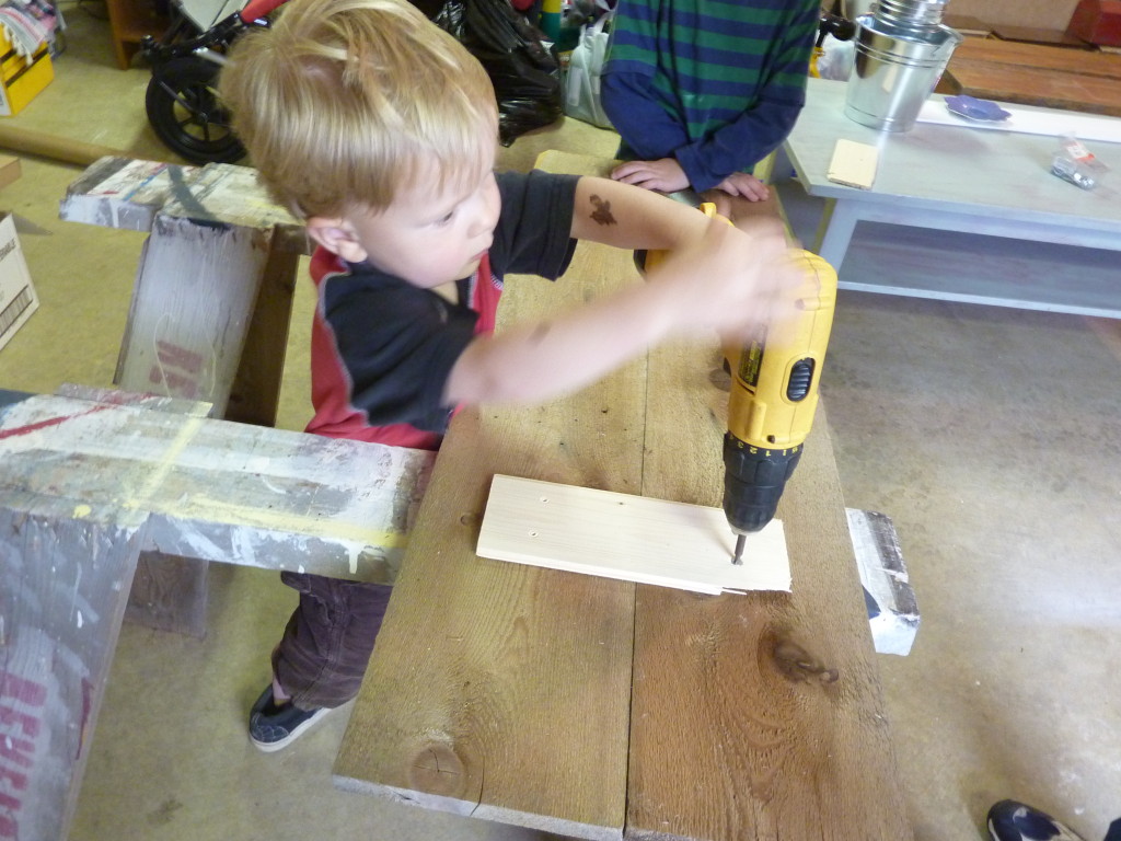 A little boy using a hand drill on a piece of wood.