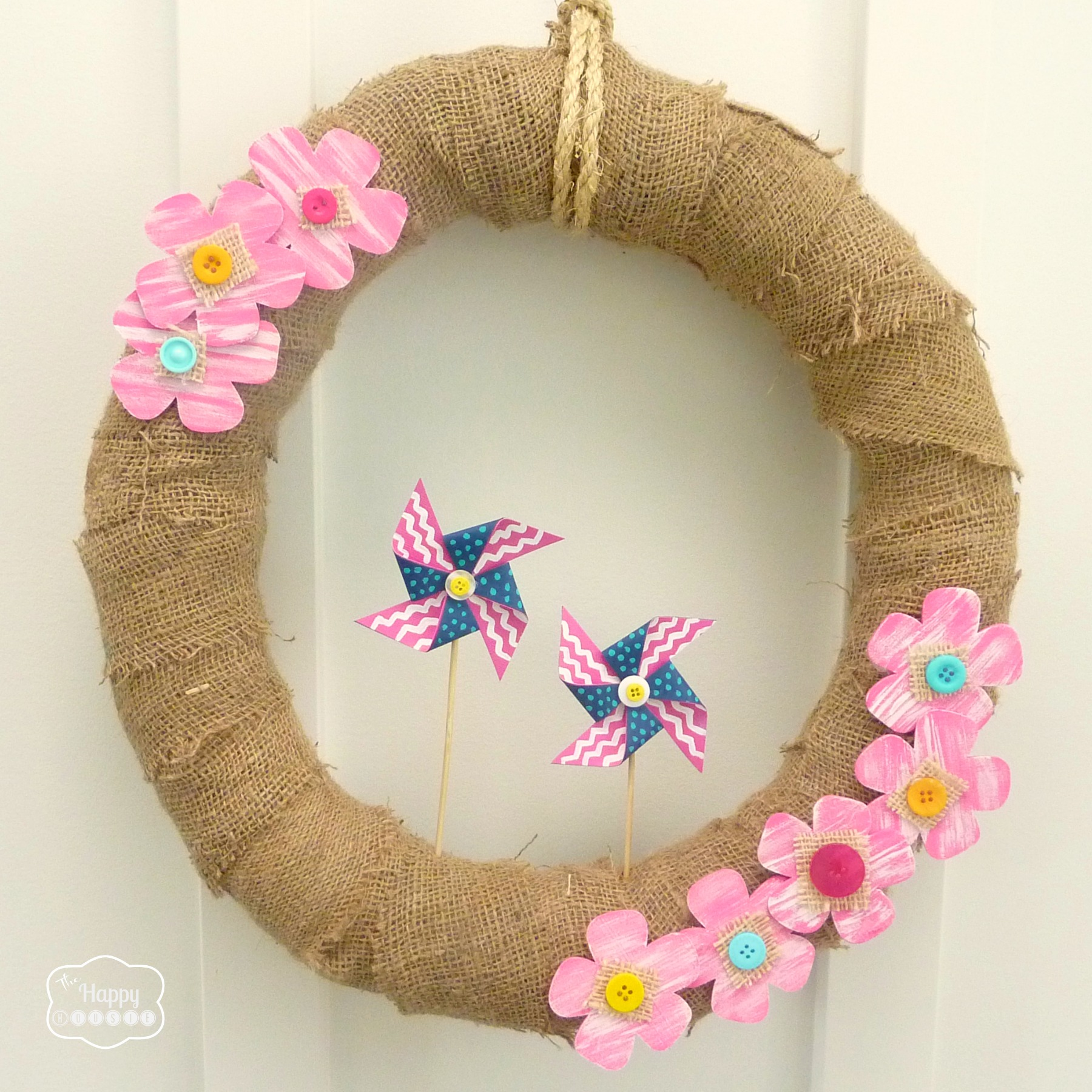 A neutral wreath with pink flowers on it, hanging on a white door.