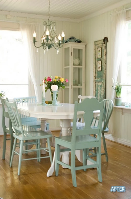 A white table with a chandelier over top of it. There are mint green chairs.