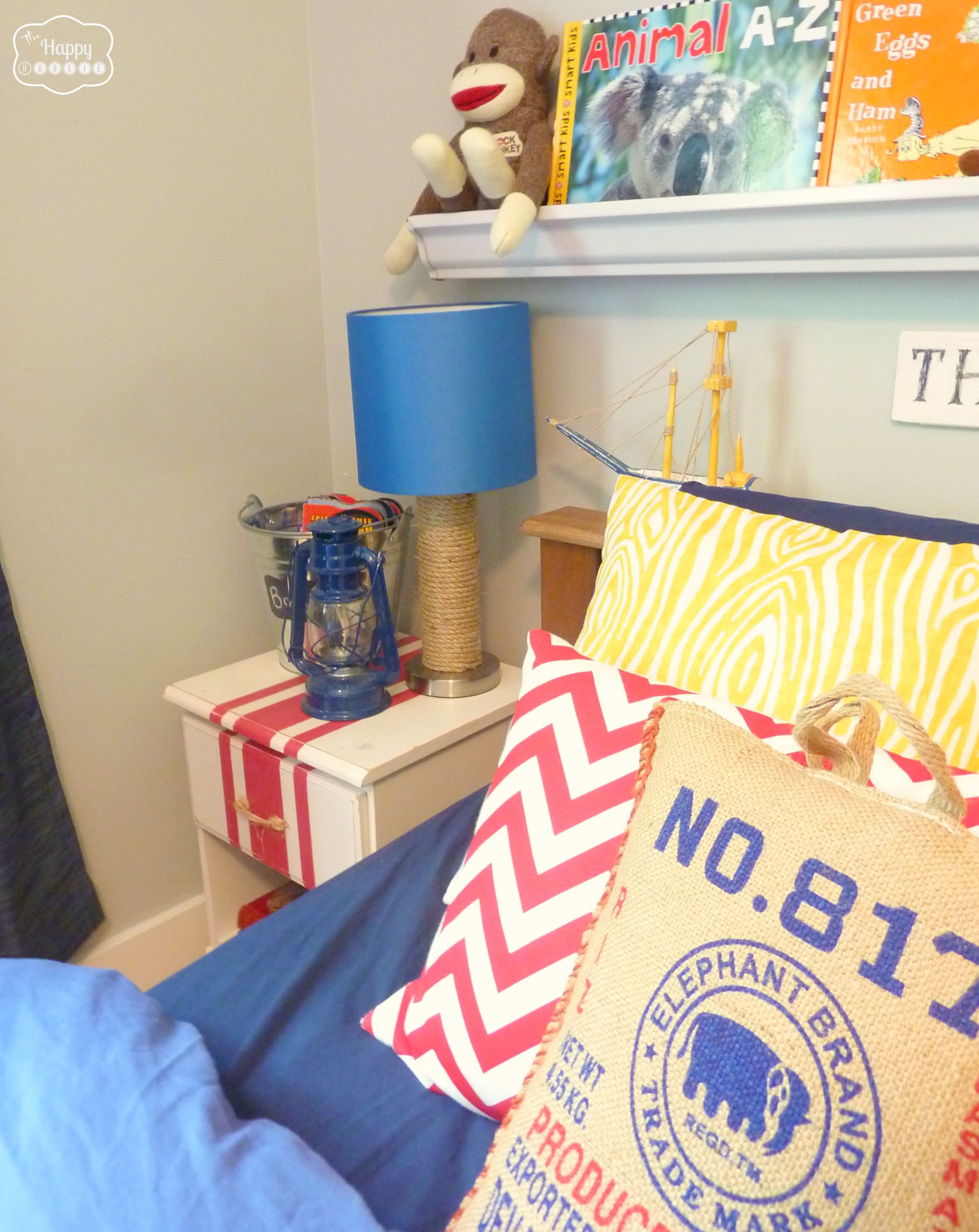A yellow, red pillow with blue sheets and the lamp beside it.