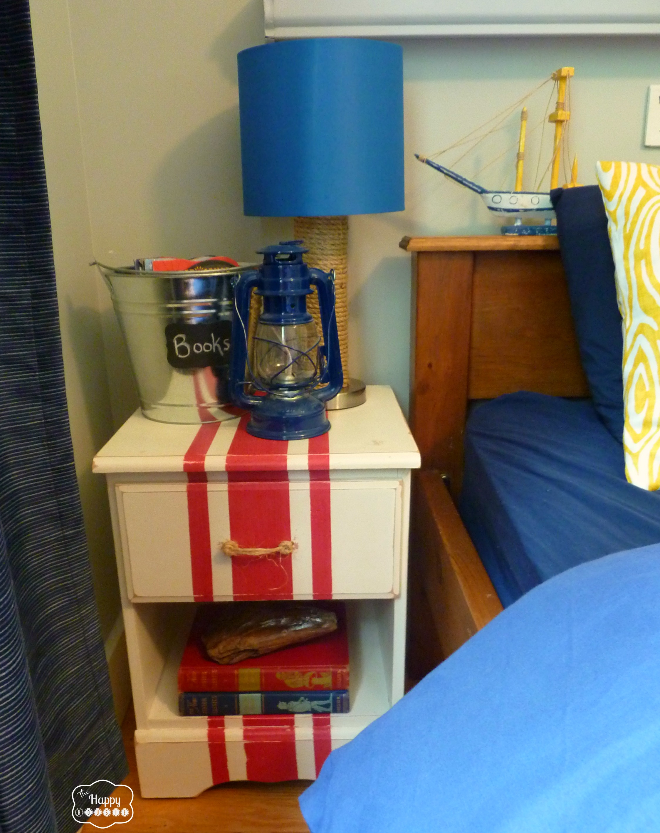 A red and white nightstand with the nautical lamp on it beside the bed.