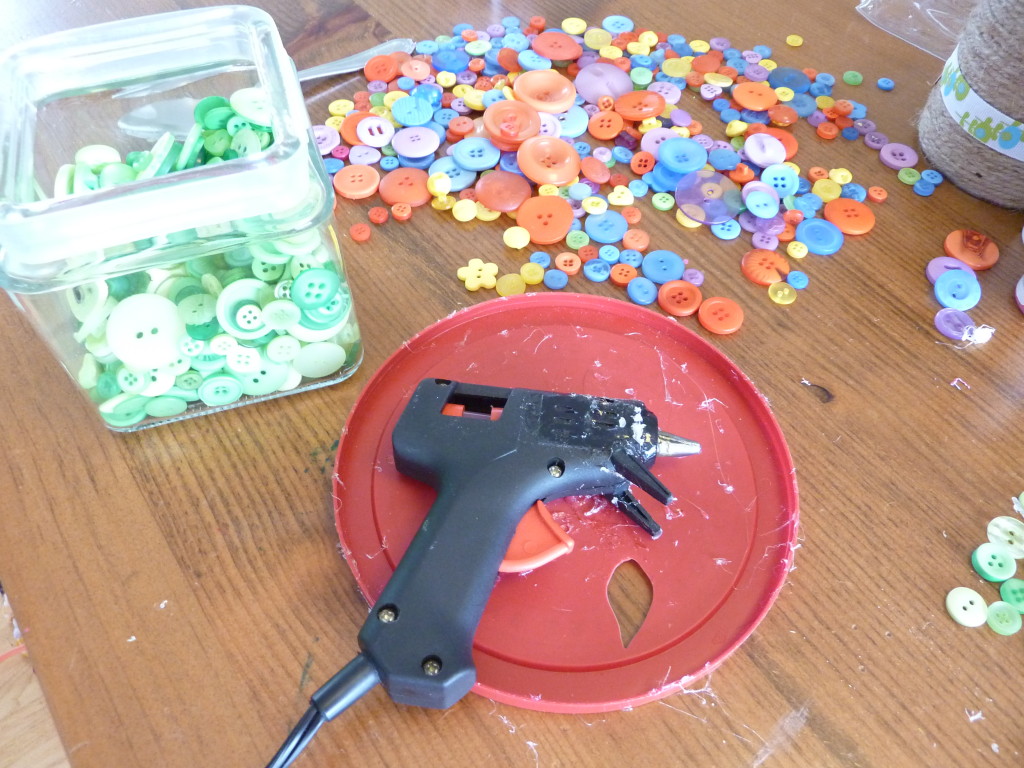 A bucket full of buttons and a hot glue gun on the counter.