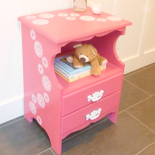 Stenciled coral pink stand with a teddy bear and books in it.