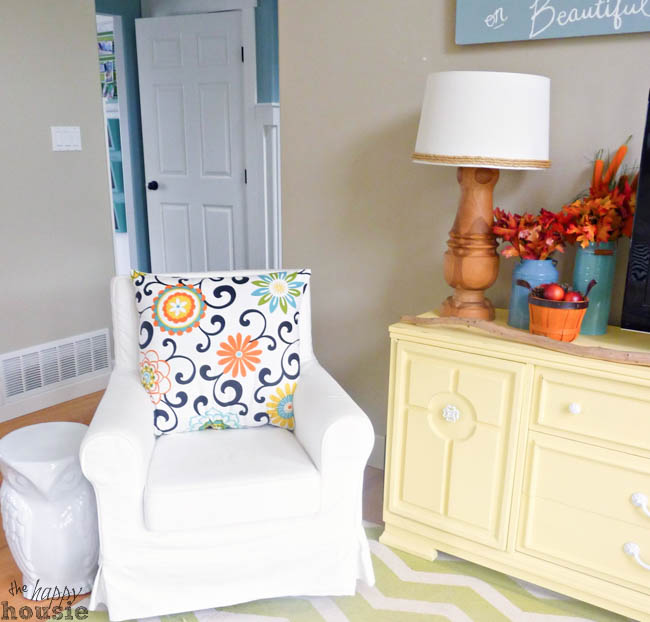 A white armchair is in the corner of the room with a flowery pillow on it.