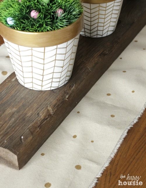 The polka dotted runner on the table with pots on top of the wooden beam.