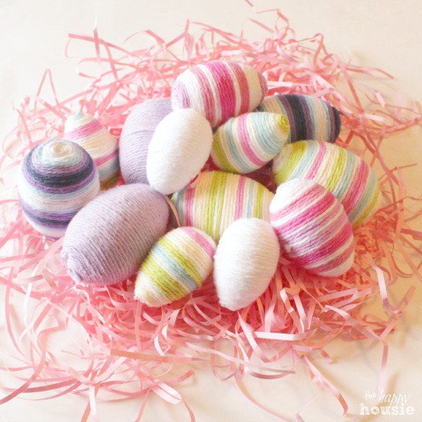 Yarn covered eggs on a bed of shredded pink paper.