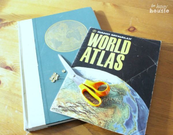 A world atlas book and scissors on top of it on the table.
