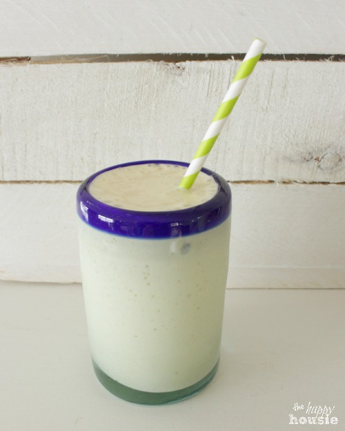 A glass with a blue rim, filled with the smoothie and a green and white straw.
