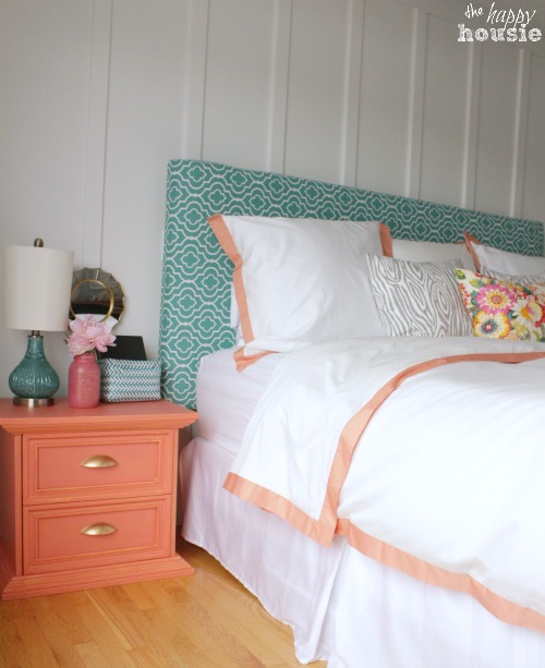 A green and white headboard with white and peach bedding.