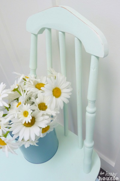 The painted chair with a vase full of daisies on it.