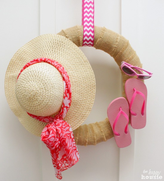 A beachy wreath with a sun hat, flip flops, and pink sunglasses on the wreath.
