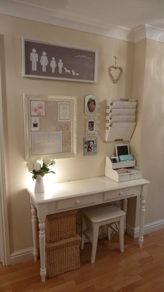 A white desk with a cork board and file folders and a small stool.