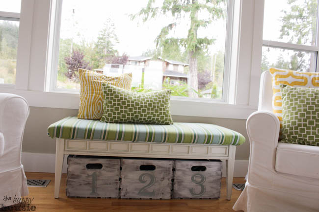 A small sitting bench with storage underneath is in front of the living room window.