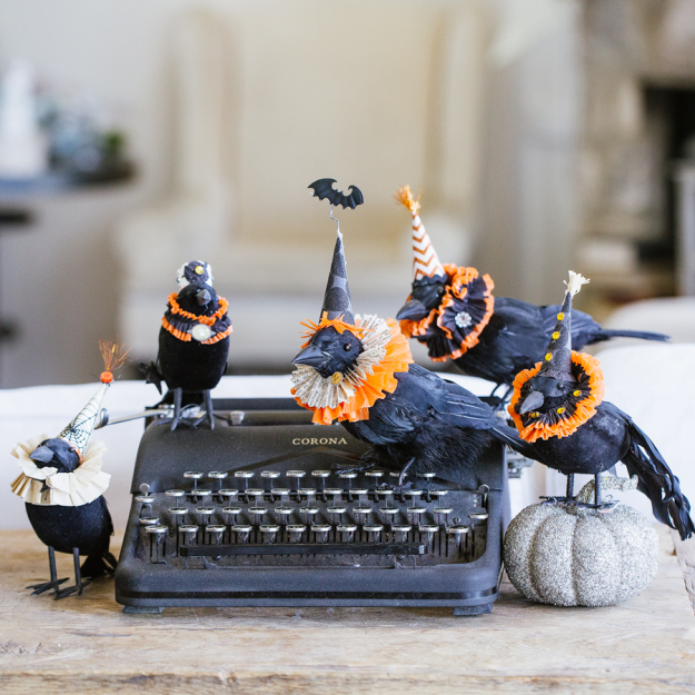 A black old typewriter with crows on top and the crows are little Halloween hats on.