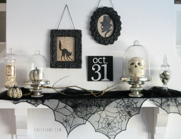 A white mantel with spider webs, and cloche's filled with skulls and pumpkins.