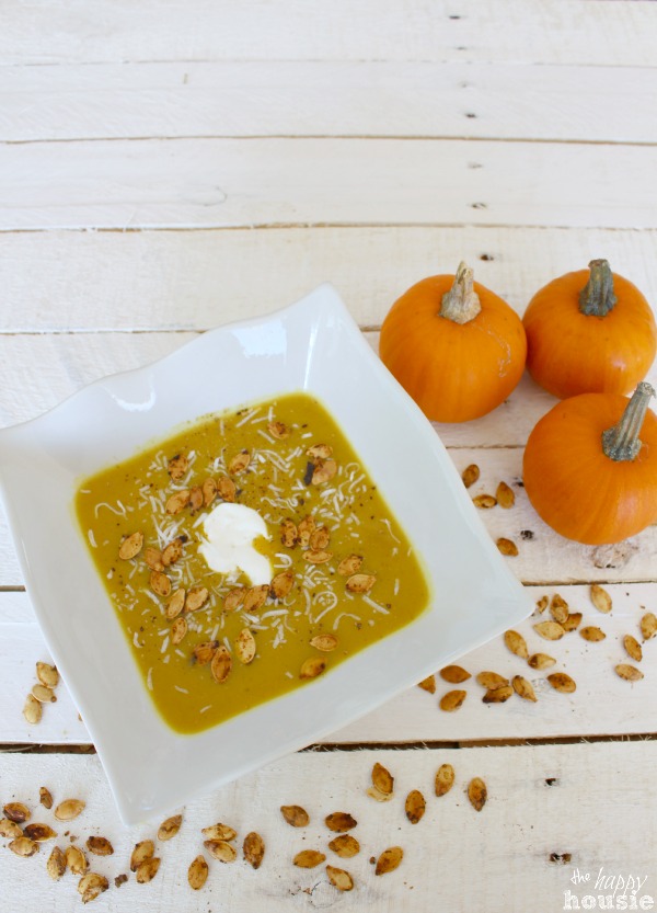 There are scattered roasted pumpkins seeds all around the white bowl full of soup.