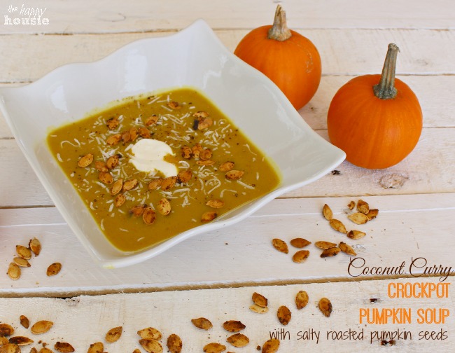 Coconut Curry Crockpot Pumpkin Soup with salty roasted pumpkin seeds on the table with two orange pumpkins beside it.