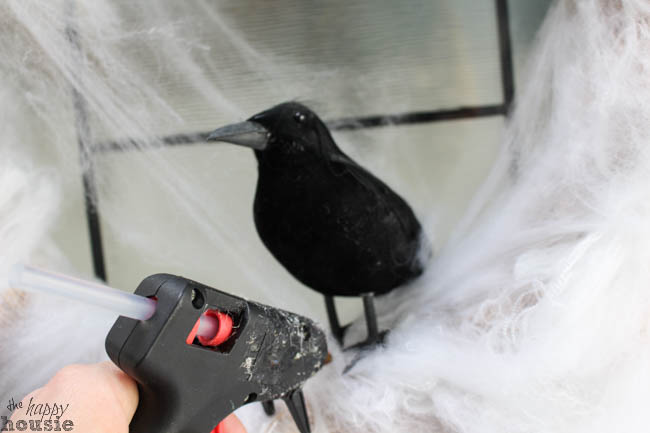 Using a hot glue gun to attach the black crow to the wreath.