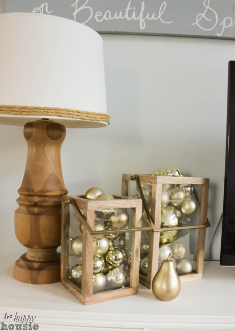 Glass wood squares filled with gold ornaments are on the side table beside a lamp.