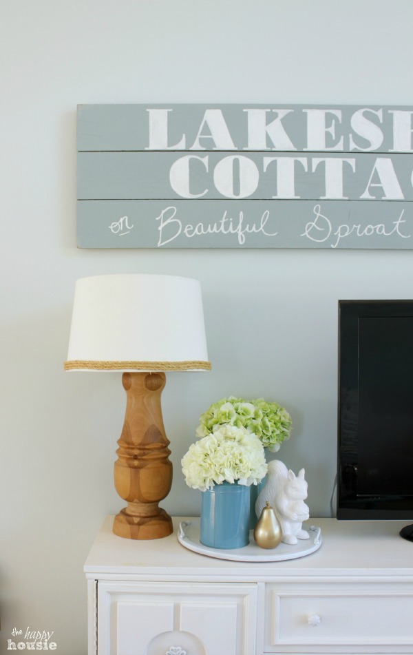 A wooden side table in living room with a TV on it, a lamp, and flowers.
