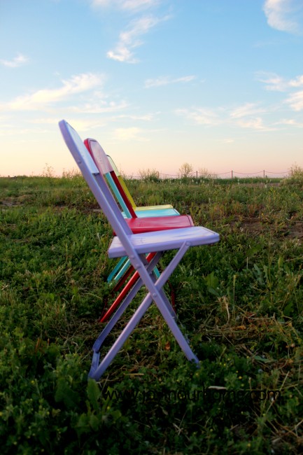 Metal chairs painted purple, red, turquoise and yellow in a field.