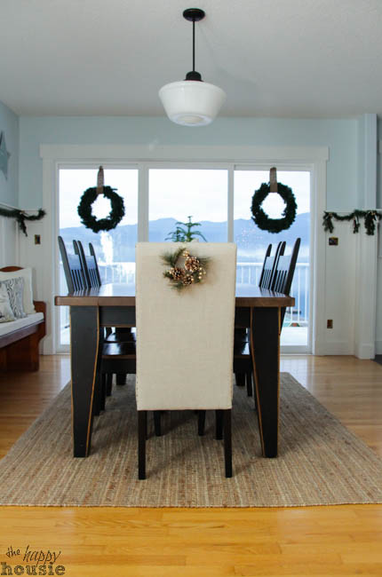 Looking at the dining room table with a small wreath on the back of the chair and wreaths on the windows.
