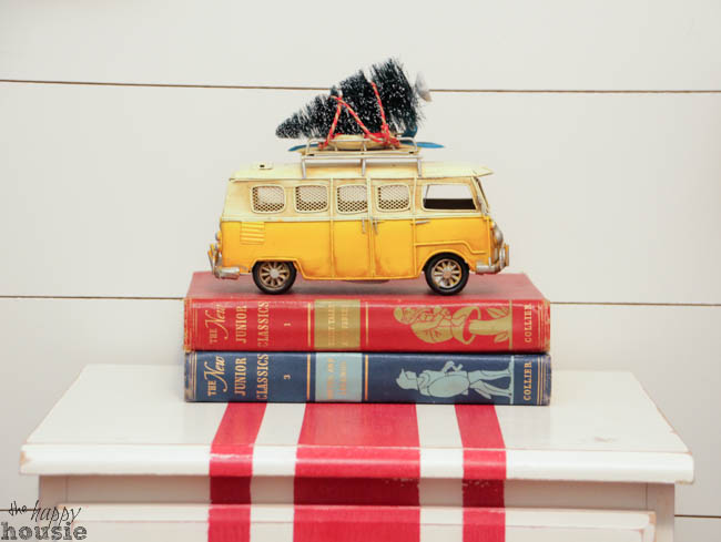 On top of a stack of books is a small van that is a toy.
