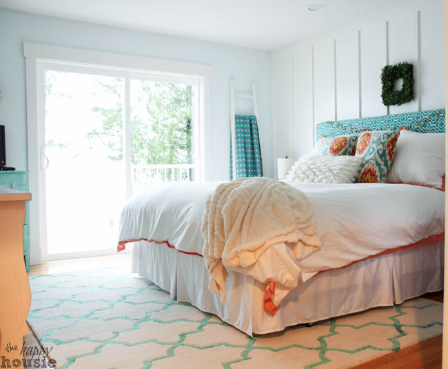 A large bed in the master bedroom beside the window with a white and orange bedspread.