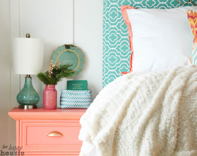Evergreen branches are in a pink vase on the peach nightstand.