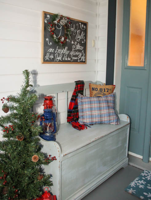 A small wooden bench just outside the front door with holiday pillows and a small Christmas tree.