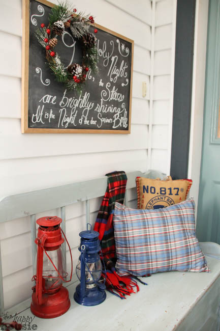 A plaid pillow, lantern and plaid throw are on the outdoor bench.