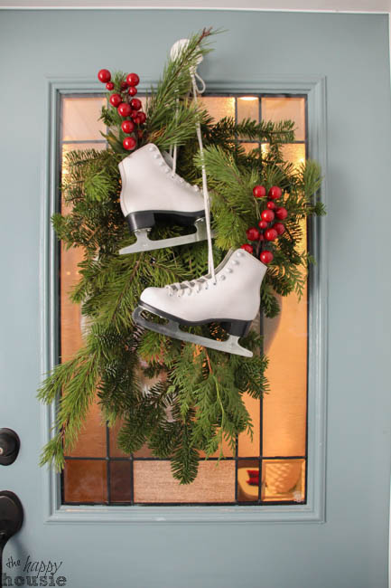 There are ice skates hanging on the front door with a holiday wreath.
