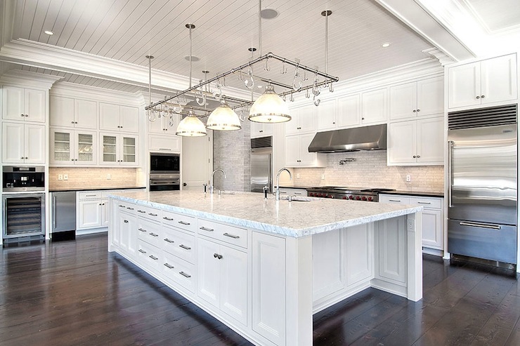 A very large white kitchen island with a rack and lights above it.