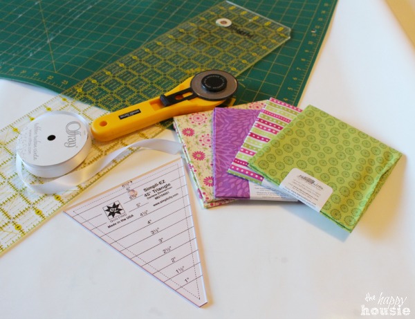 A triangle shape, fabric, a cutting tool, and measuring device on the counter ready to sew.