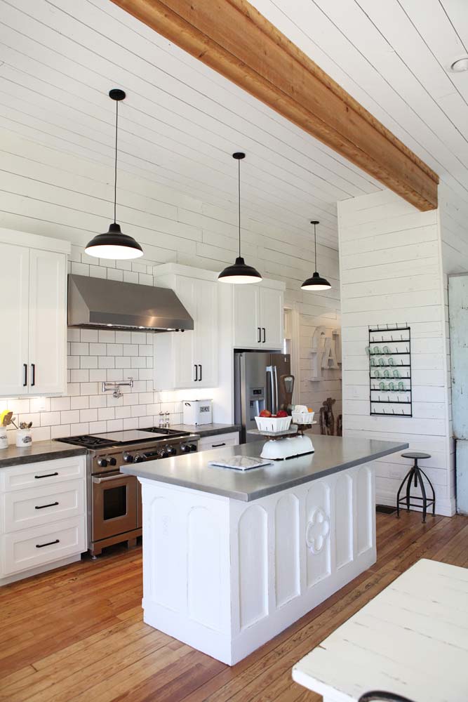 All white kitchen with pops of black and a wooden beam on the ceiling.
