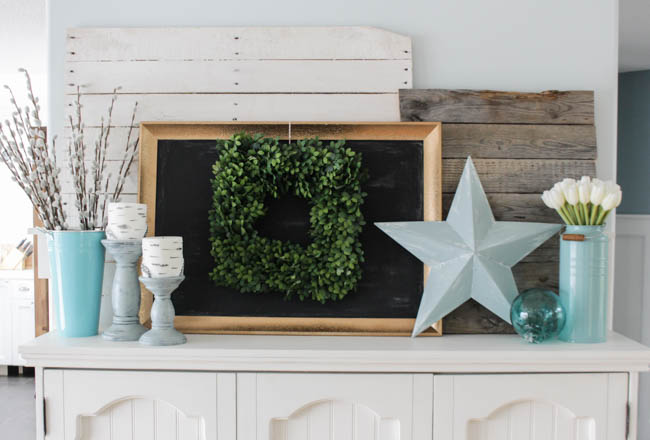 There is a green wreath on a chalkboard on the sideboard.