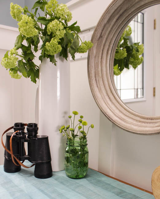 Binoculars, a round mirror and a white vase is on the table. 