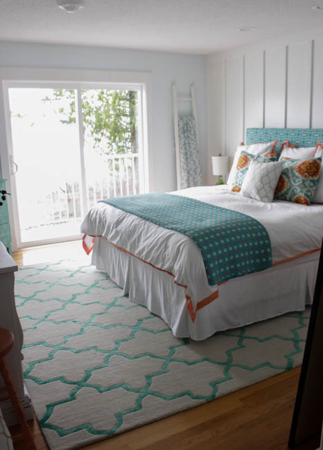 A large bed is in the master bedroom with aqua and orange pillows.