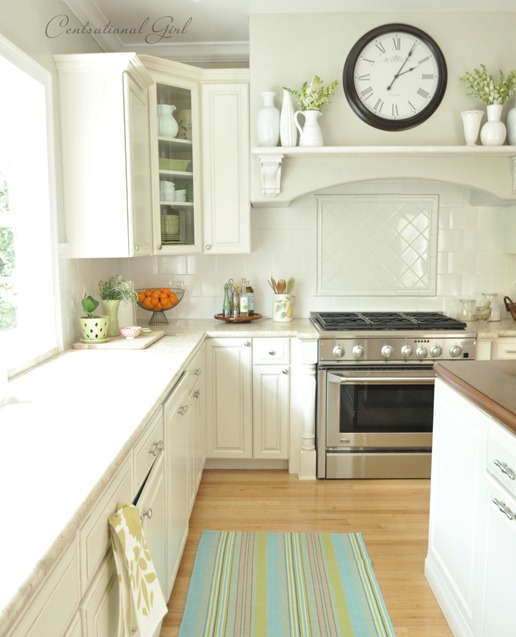 A white kitchen with a large round clock over the hood fan.