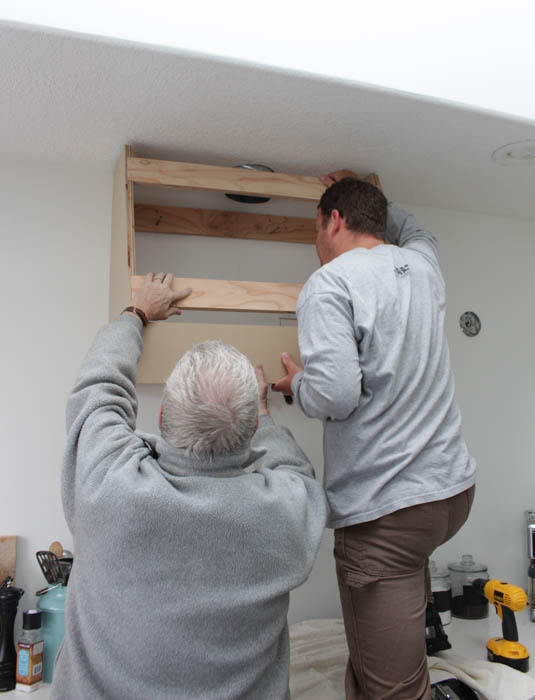 Two men holding the hood range up to install.