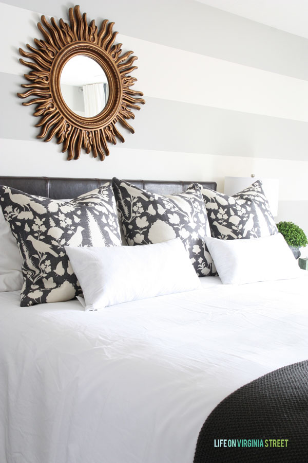 Black and white DIY pillows on a bed with a sunburst mirror on the wall.
