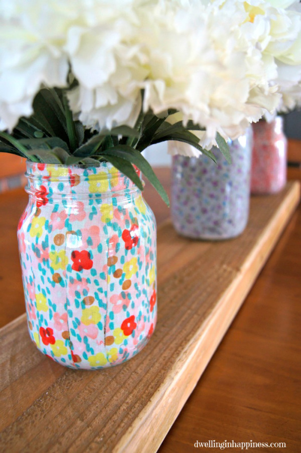 Mason jars covered in spring fabric with white flowers in them.