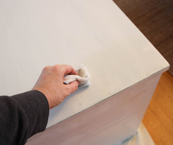 Rubbing the painted dresser with a cloth.