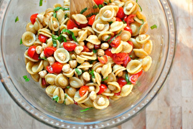 Caprese-Pasta-Salad-in a clear glass bowl with a wooden spoon.