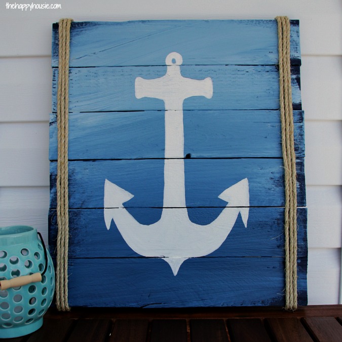 A pallet painted blue with a white anchor and nautical rope sign leaning up on the dock.