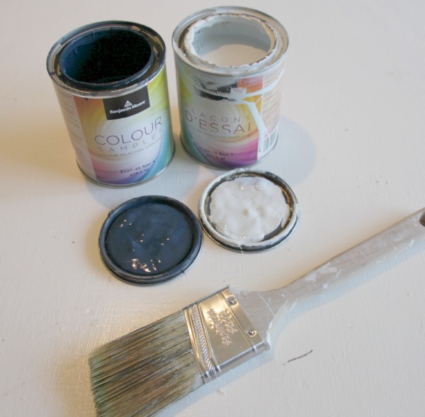 Cans of blue and white paint with a brush beside it.