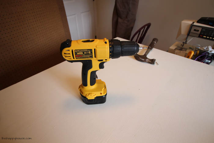 A yellow drill on the table with a hammer beside it.