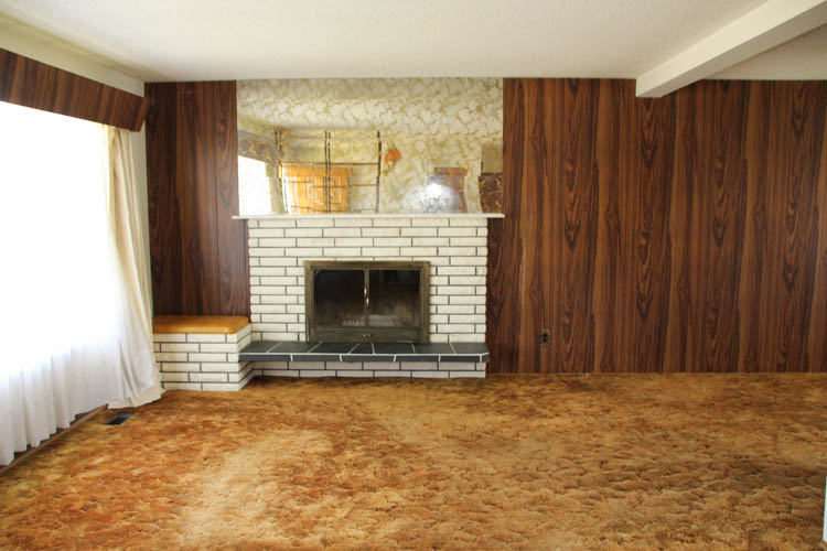 A very dated looking fireplace surrounded by wood paneling in the living room.