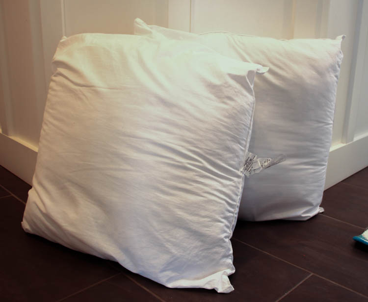 Two giant pillow inserts on the floor by a wall.