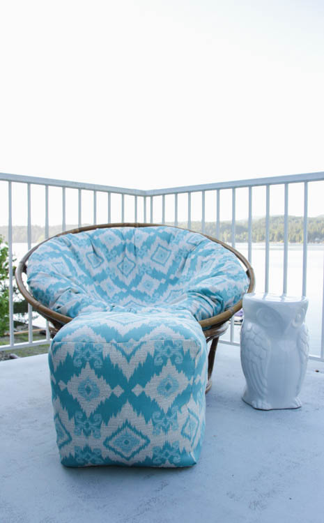 The white and blue papasan fabric covered chair with a white owl table beside it on the porch outside.